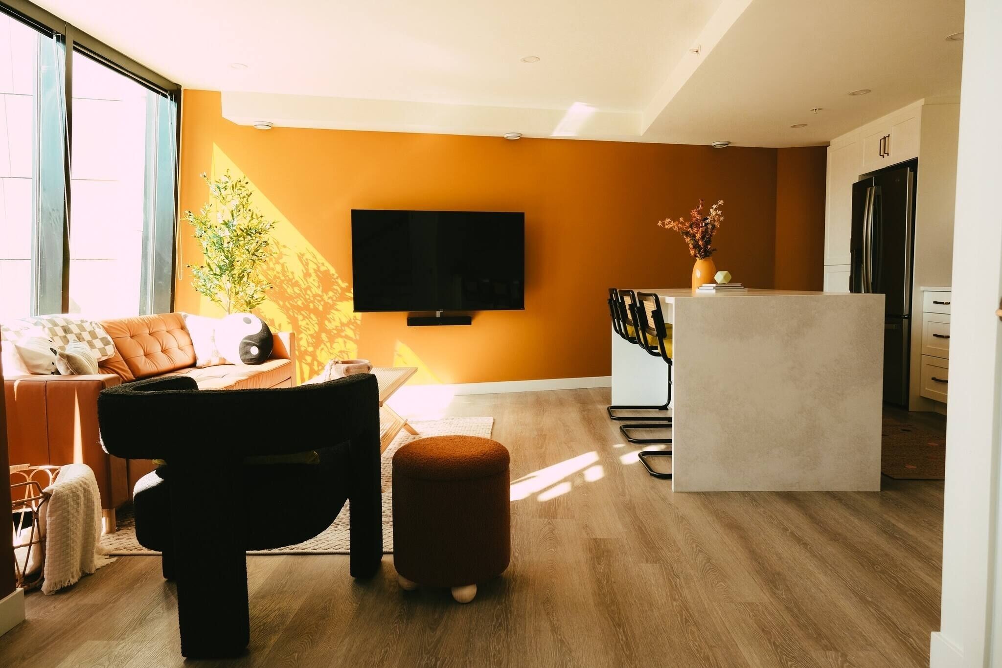 A modern living room with a sofa, ottoman, and a flat-screen TV mounted on the wall.