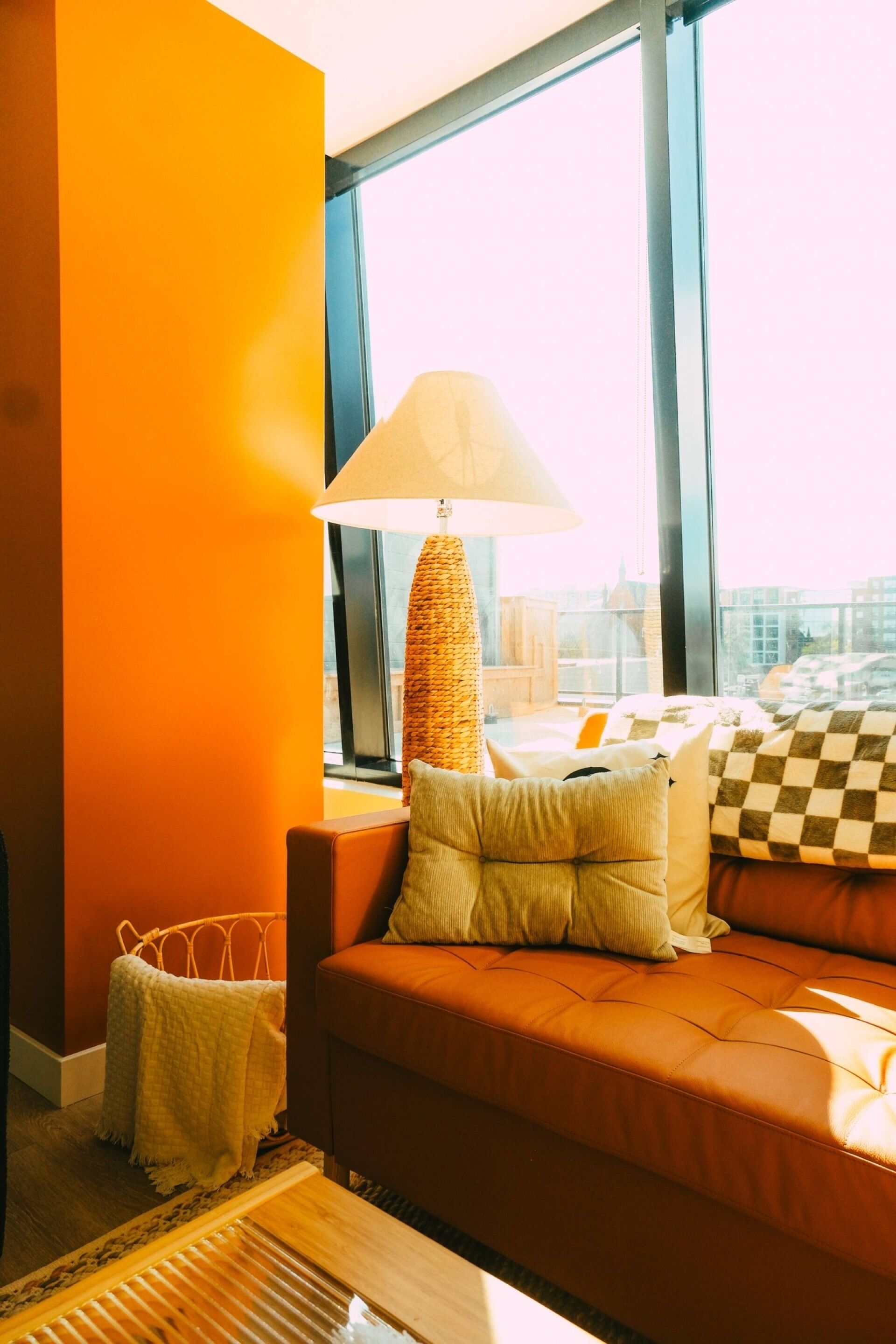 A modern living room with a sofa, a lamp, and a view of the city through large windows.