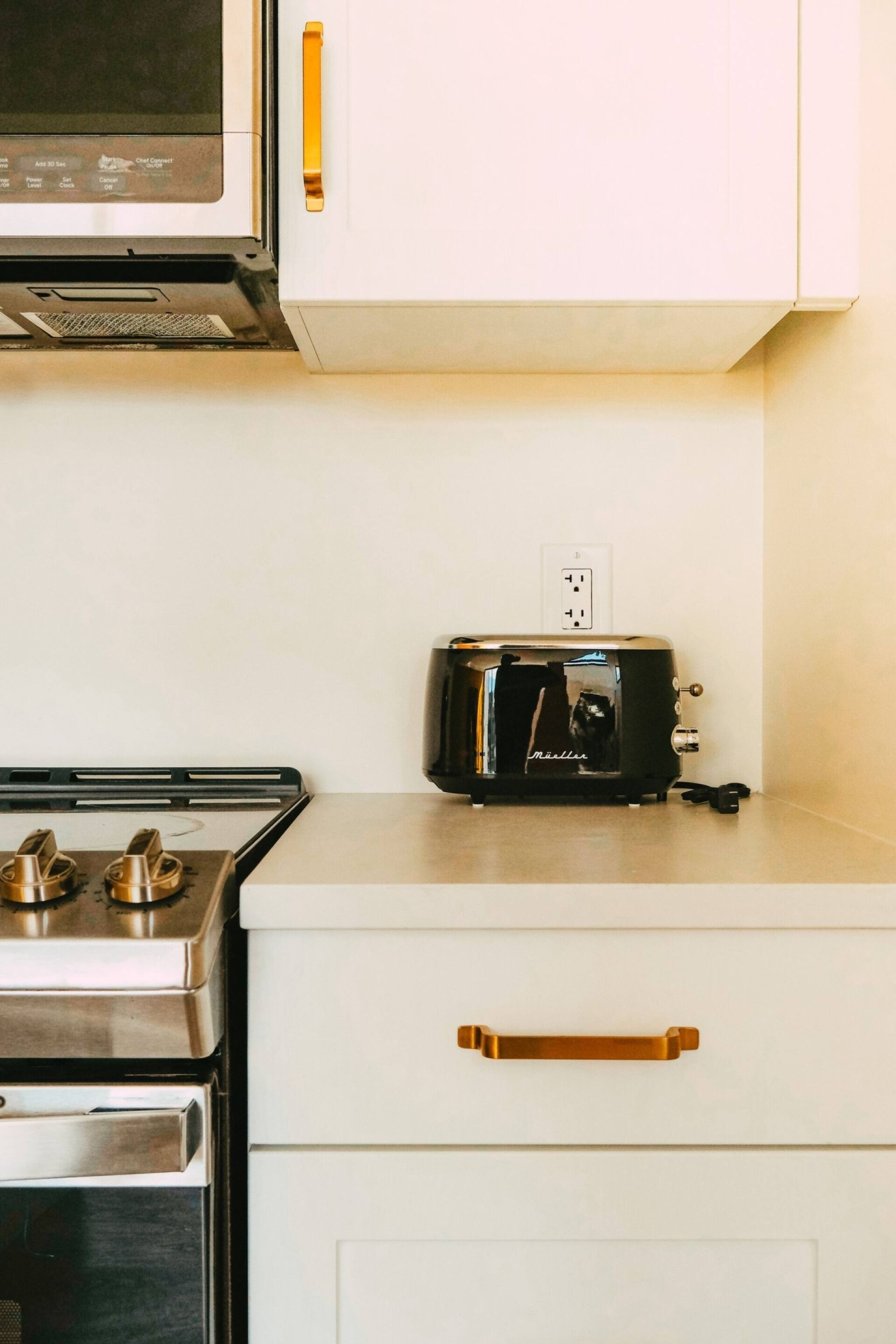 Una cucina con microonde, tostapane, fornello e un cassetto con maniglia dorata.