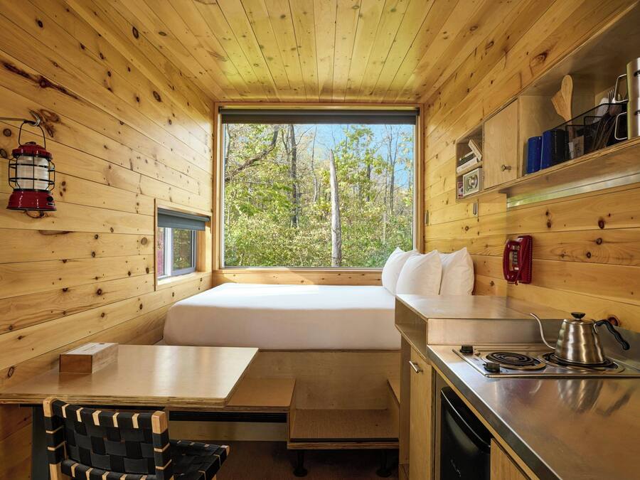 A cabin interior with a wooden interior, a window seat, a kitchenette, and a dining area.