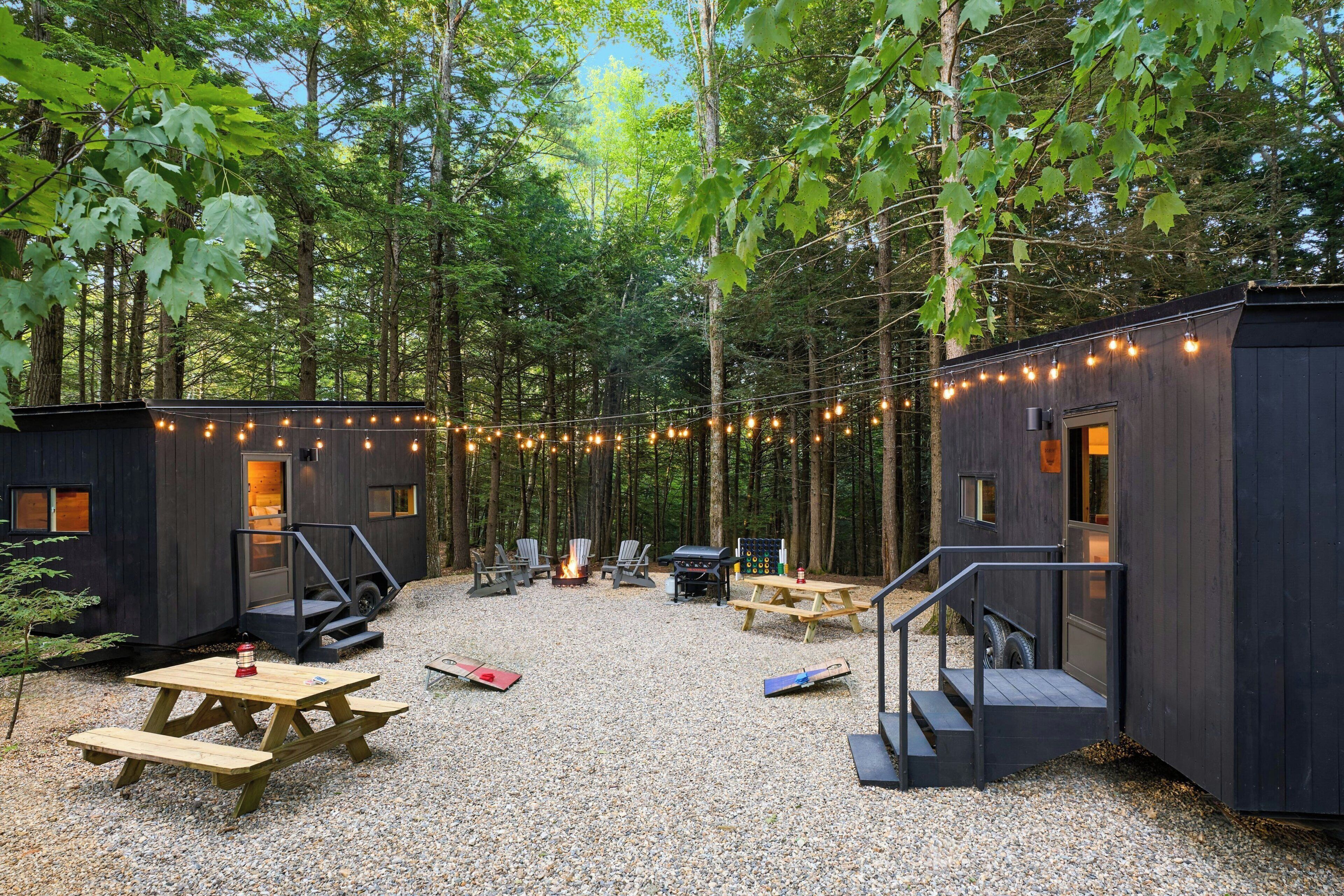 A forested campsite with two cabins, outdoor seating, and a fire pit.