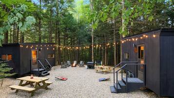 A forested campsite with two cabins, outdoor seating, and a fire pit.