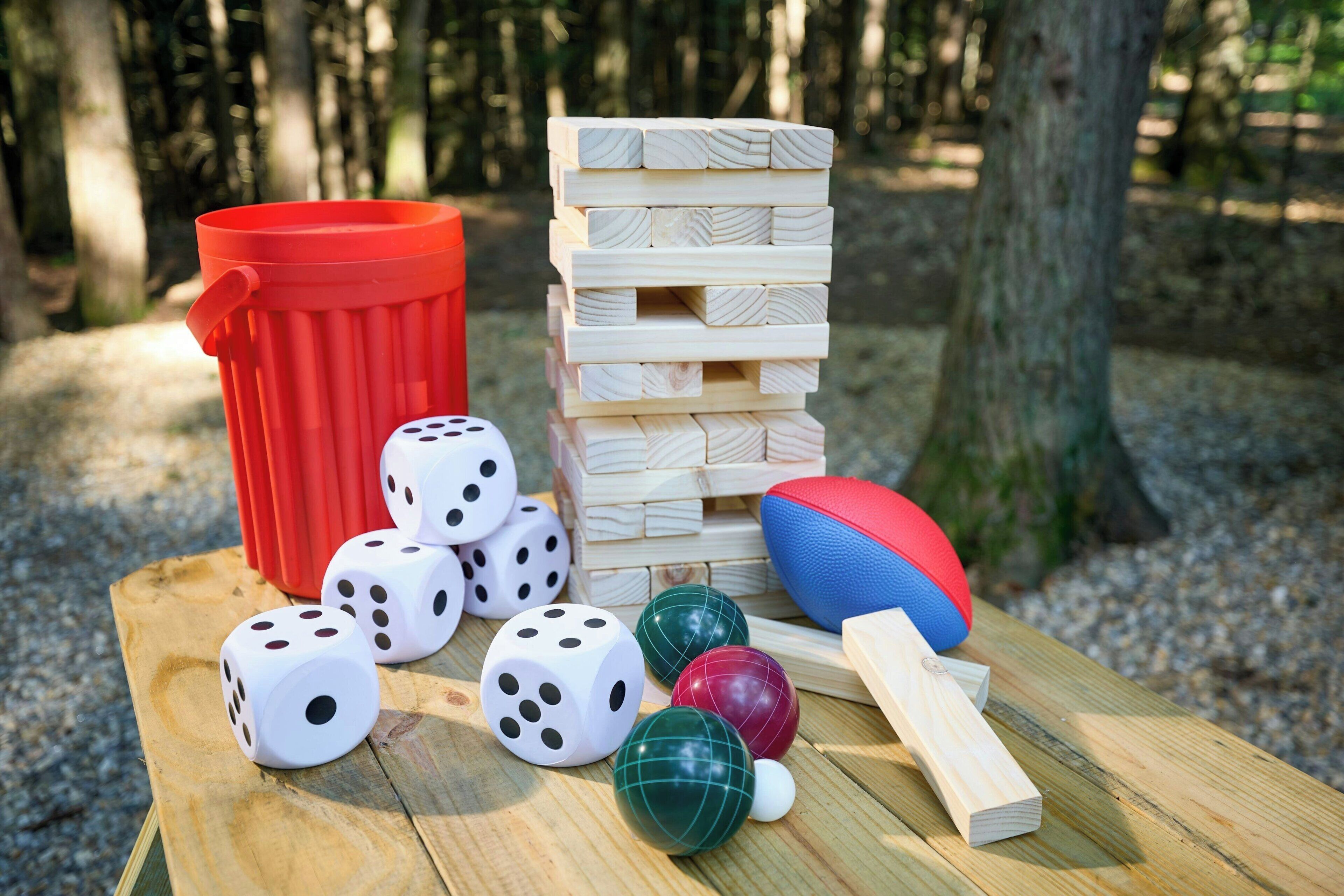 A wooden table with dice, a jenga tower, a red bucket, and a ball.