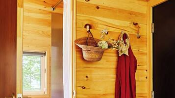 A wooden room with a shower, a small window, a basket with flowers, and a pair of shoes on the floor.
