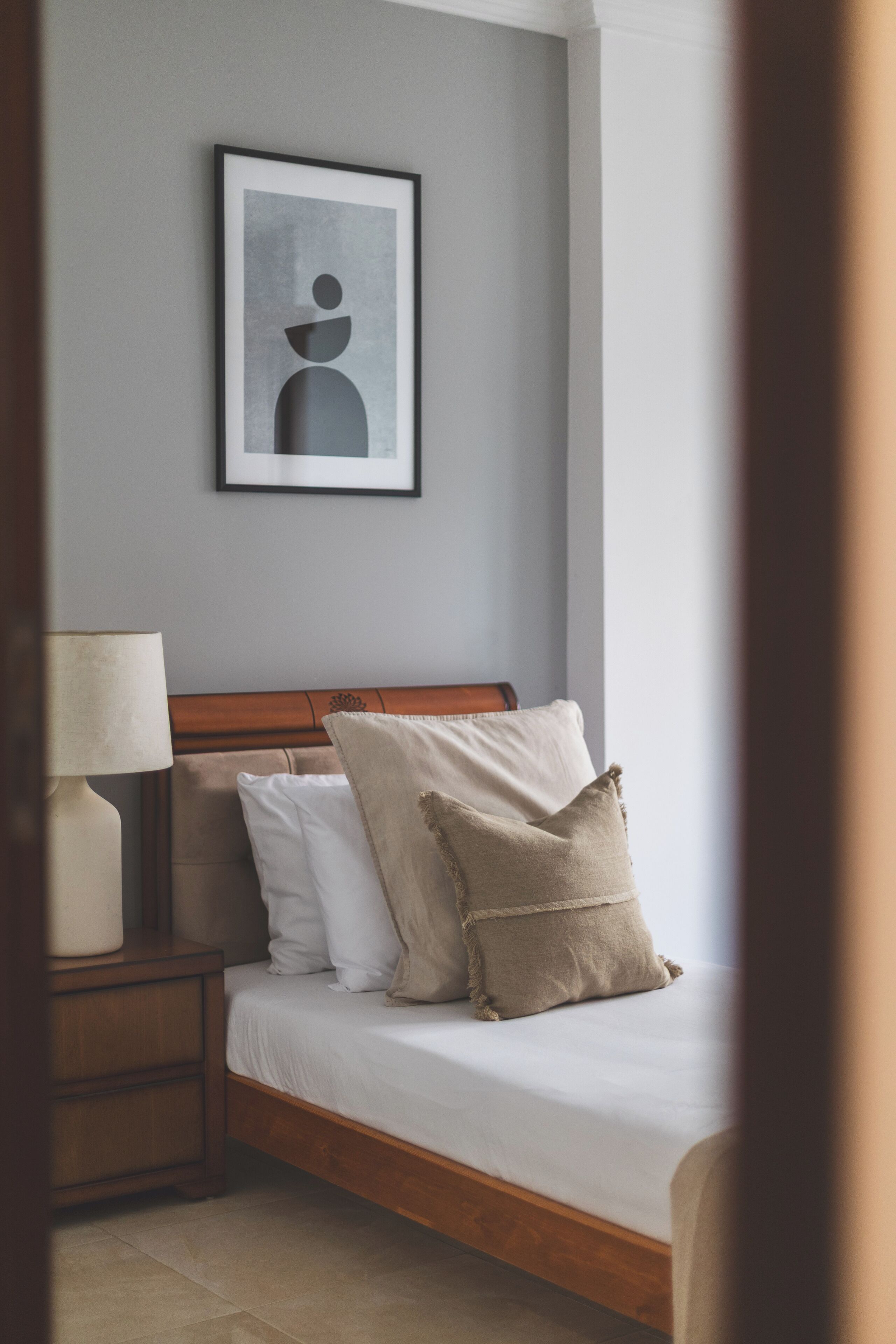 A neatly made bed with white and beige pillows, a wooden headboard, and a framed picture on the wall.