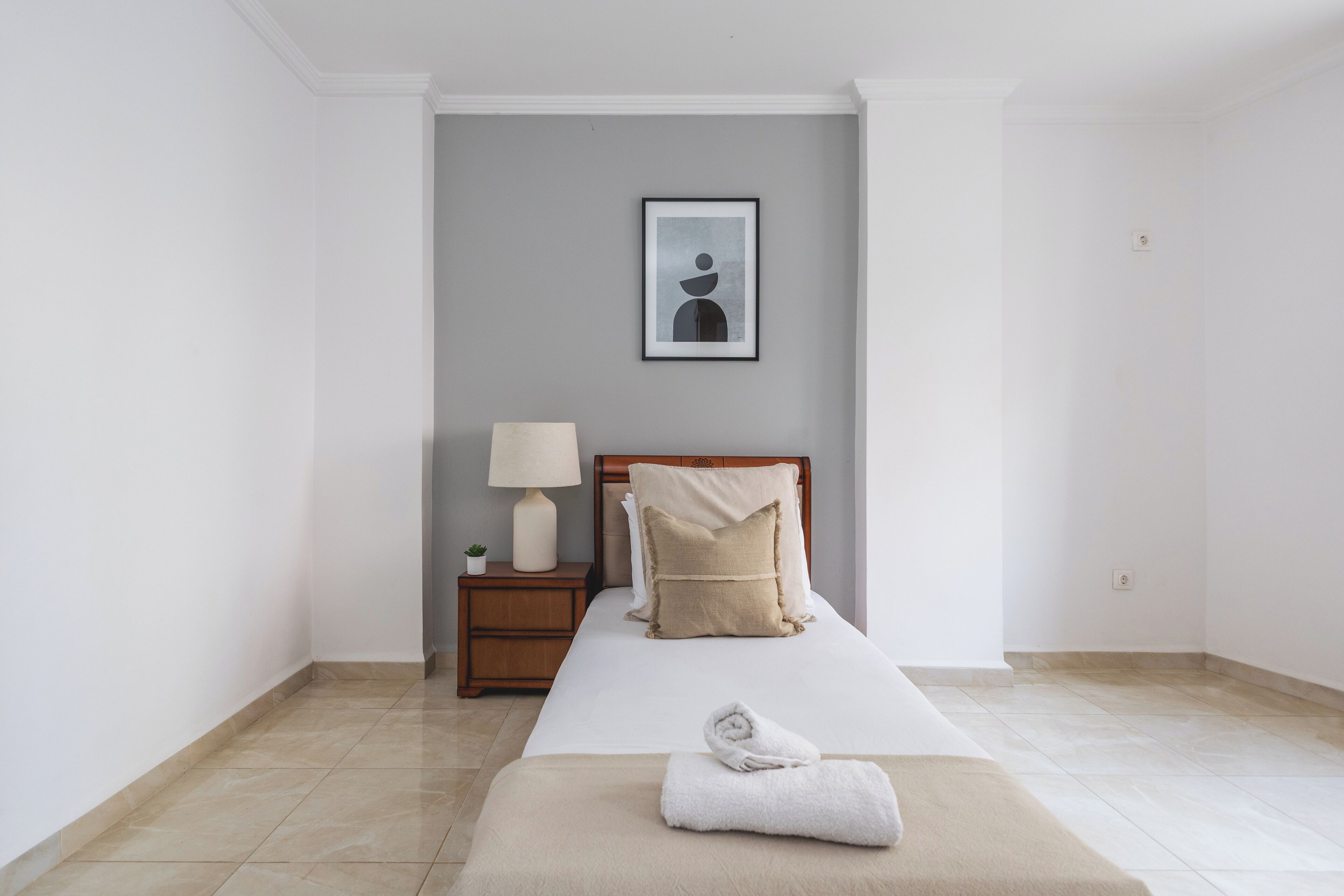 Habitación de hotel con cama, mesita de noche con lámpara y un cuadro en la pared.