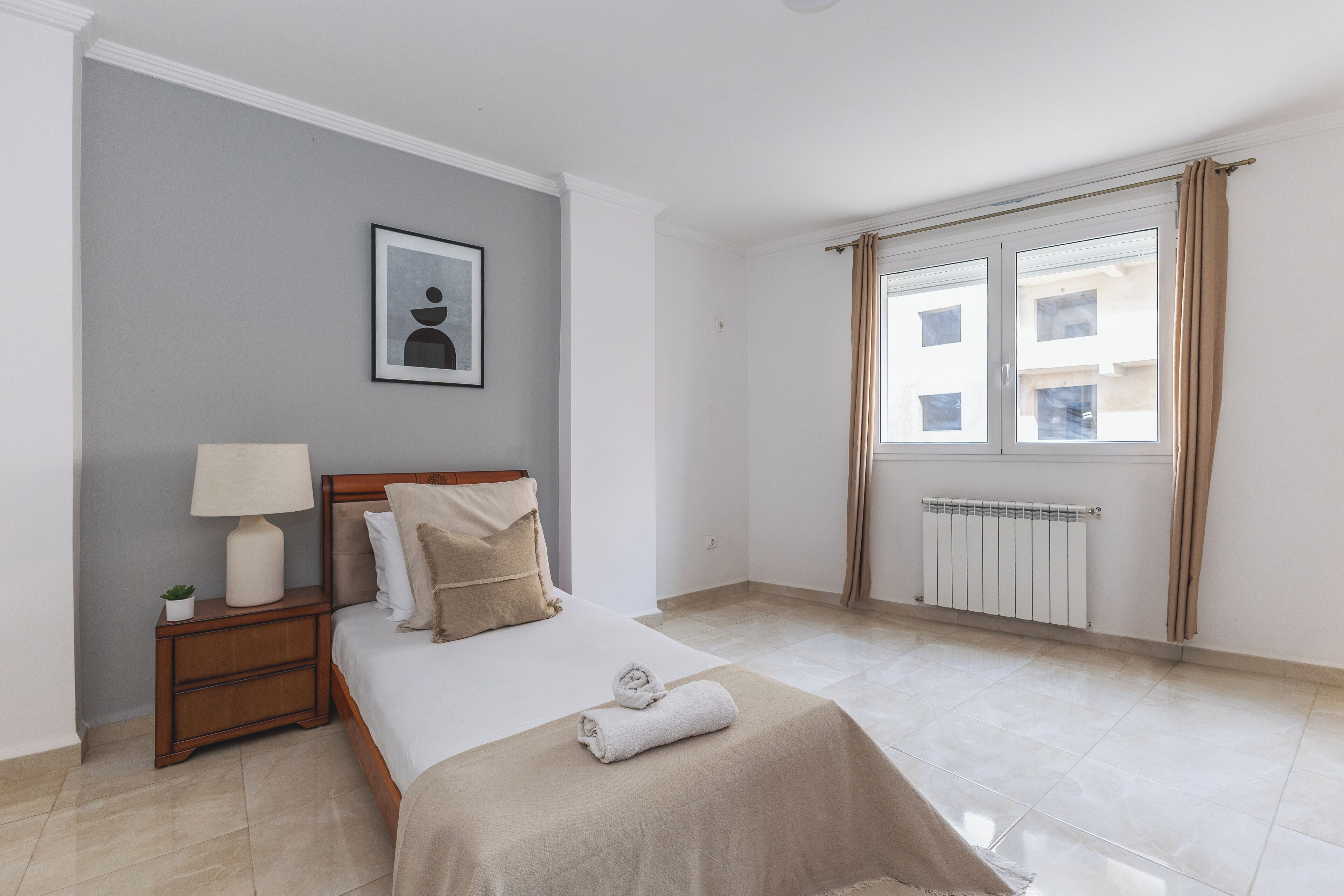 A neatly arranged bedroom with a bed, bedside table, lamp, and a window with curtains.