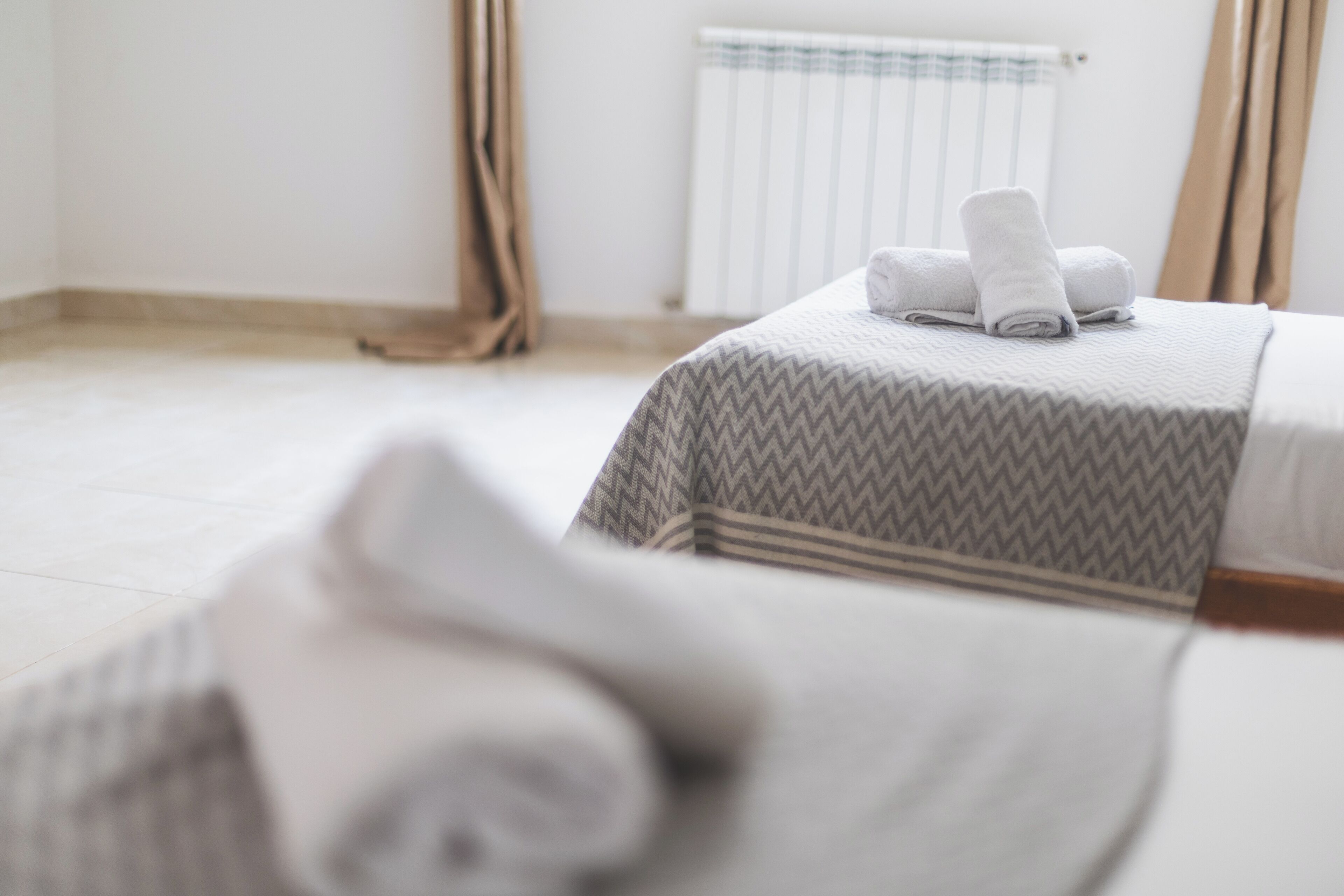 A neatly made bed with a patterned bedspread and rolled towels on top.