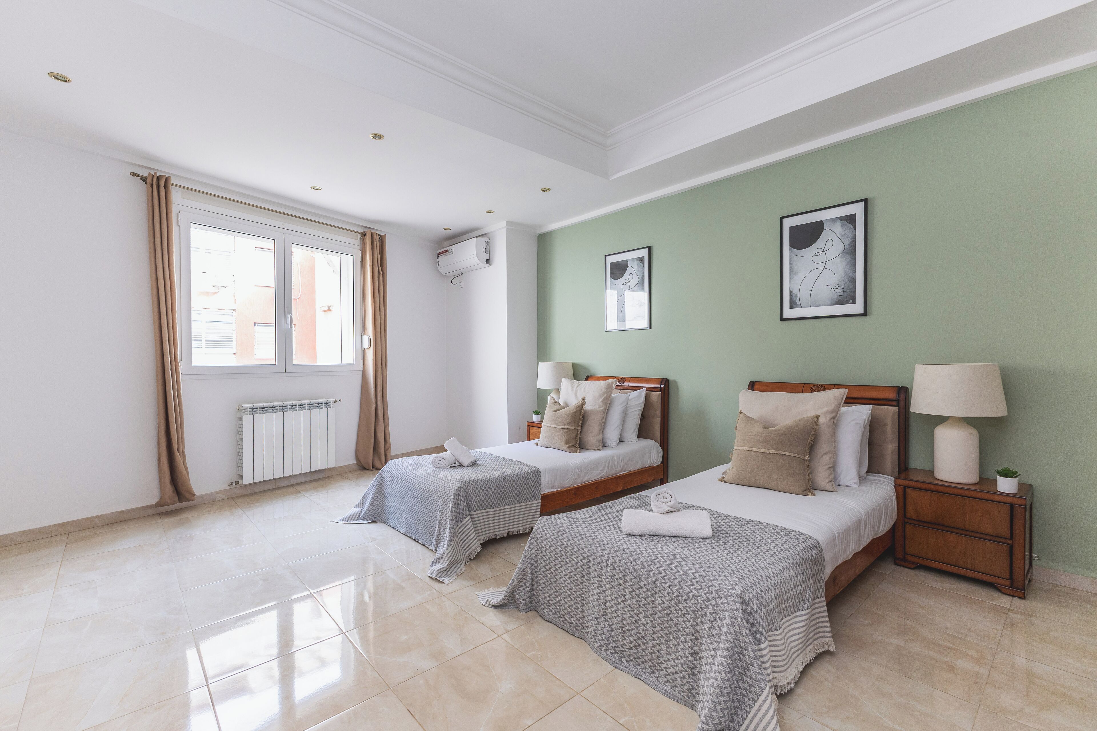 Habitación de hotel con dos camas, una ventana con cortinas, un radiador y un aire acondicionado instalado en la pared.