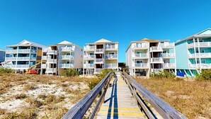 A boardwalk leading to beachfront buildings with balconies and a clear sky.