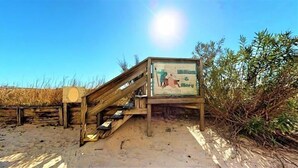 A wooden staircase leading to a beach area with a signboard.