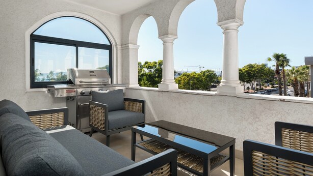 Un balcon équipé d’un barbecue, de sièges et offrant une vue sur le paysage urbain.