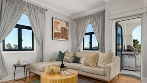 Un salon spacieux avec un canapé beige, une table basse ronde en bois et une grande fenêtre agrémentée de rideaux.