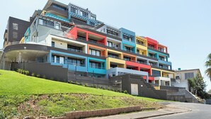 A multi-story residential building with balconies, a landscaped lawn, and a clear sky.