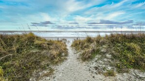 Ein Strandweg, der zum Meer führt, mit blauem Himmel.