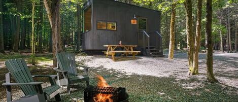 A cabin with a fire pit, outdoor seating, and a gravel ground.