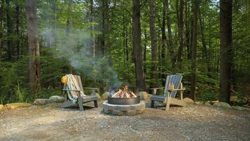 Un feu de camp avec deux chaises Adirondack dans une forêt.