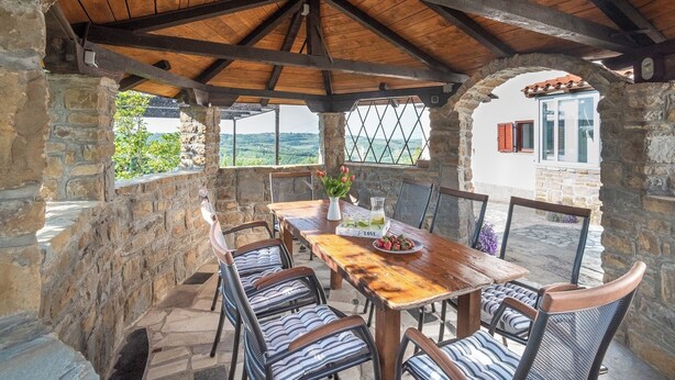A rustic outdoor dining area with stone walls, wooden beams, and a view of the countryside. - Boutique House Rustikana with pool Korte (Izola)