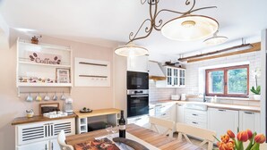 A modern kitchen with white cabinets, a wooden dining table, and a chandelier. - Boutique House Rustikana with pool Korte (Izola)