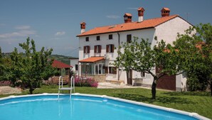 A pool area with a white building in the background, a ladder leading into the pool, and a tree in the foreground. - Boutique House Rustikana with pool Korte (Izola)