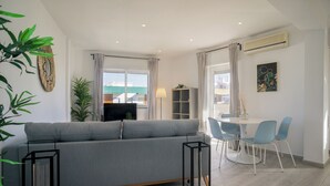 A modern living room with a grey sofa, a dining table with blue chairs, and a bookshelf. - Linaria Apartment, Portimão, Algarve (Portimão)