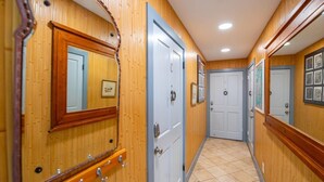 A hallway with wooden paneling, a tiled floor, and doors with mirrors and artwork. - Yellowfin Ledge | Ideal Getaway On Duval! Balcony (Key West)