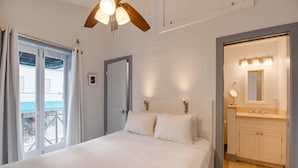 A bedroom with a bed, a ceiling fan, a window with curtains, and a bathroom with a sink and mirror. - Yellowfin Ledge | Ideal Getaway On Duval! Balcony (Key West)