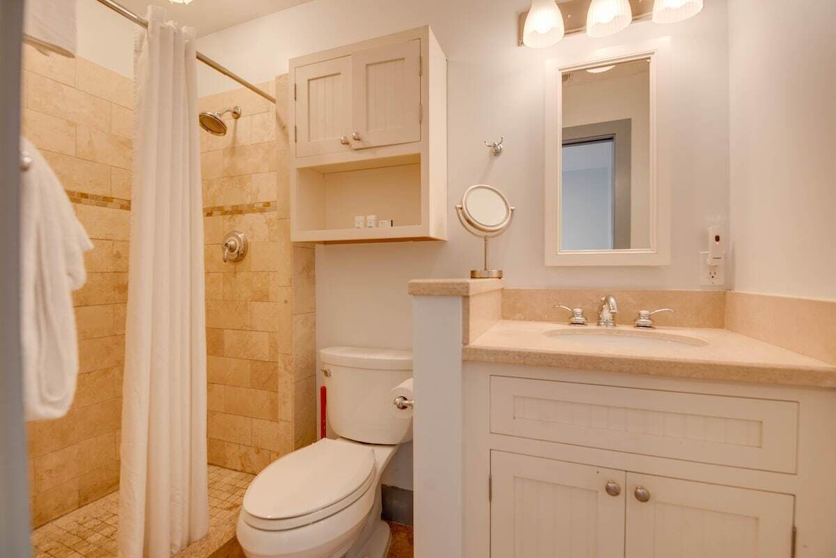 A bathroom with a shower, toilet, vanity with a mirror, and cabinets.