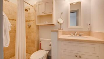 A bathroom with a shower, toilet, vanity with a mirror, and cabinets.