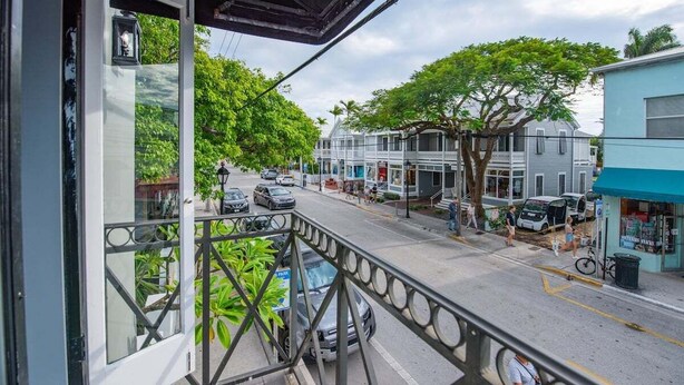 A balcony with a view of a street lined with trees and parked cars. - Yellowfin Ledge | Ideal Getaway On Duval! Balcony (Key West)