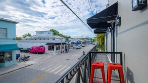Straatbeeld met een gebouw, een balkon met rode krukken, een roze bestelwagen en een yogawinkel.