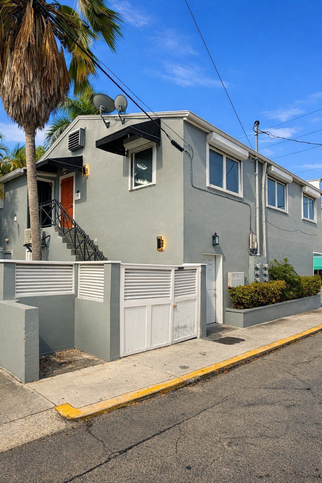 A two-story residential building with a grey exterior, a red door, and a satellite dish.