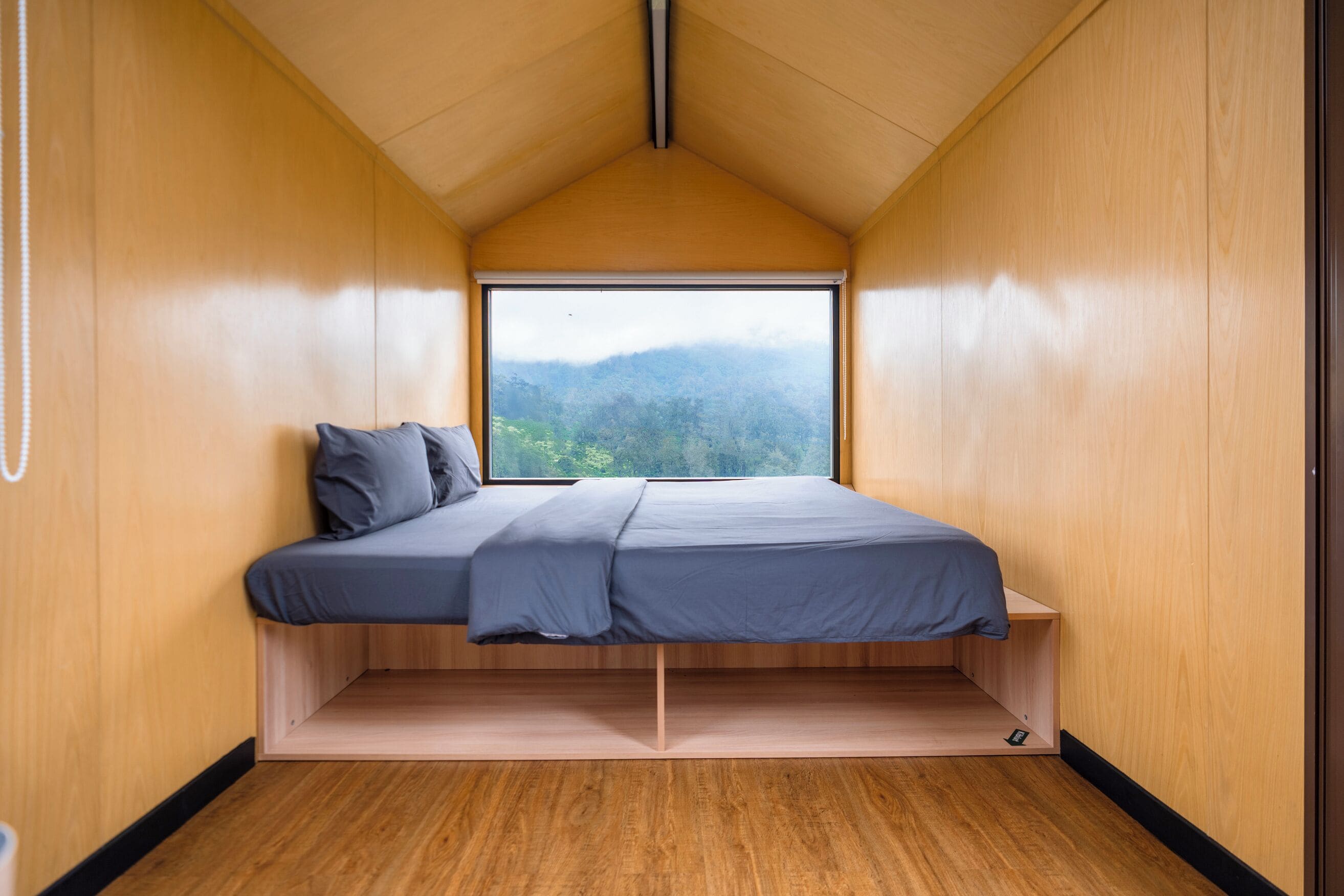 A compact room with a bed, a window, and a view of a forest.