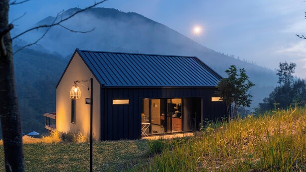 Een modern huis met een donker dak, grote ramen en een zichtbaar interieur met een eethoek.