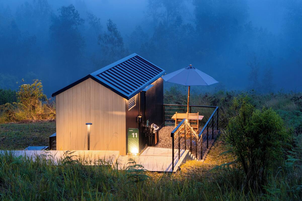 Une cabane avec une façade en bois, une petite véranda et une table avec un parasol.