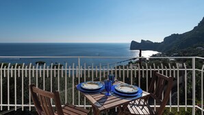 A table with plates and blue glasses on a balcony overlooking a coastal view with a rocky outcrop. - MAIN Roof Terrace Apartment (Massa Lubrense)