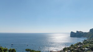 A coastal view with boats on the water, a rocky coastline, and a village with buildings. - MAIN Roof Terrace Apartment (Massa Lubrense)