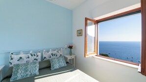 A bedroom with a bed, a nightstand, a vase with flowers, and a window with a view of the sea. - MAIN Roof Terrace Apartment (Massa Lubrense)