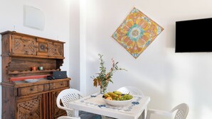 A dining area with a wooden cabinet, a table with a fruit bowl, white chairs, and a decorative tile on the wall. - MAIN Roof Terrace Apartment (Massa Lubrense)