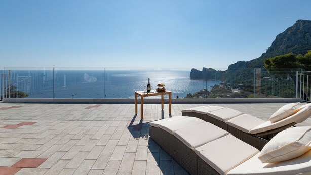 A terrace with a view of the sea, a table with a bottle and fruit, and lounge chairs. - MAIN Roof Terrace Apartment (Massa Lubrense)