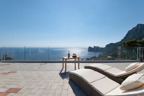 A terrace with a view of the sea, a table with a bottle and fruit, and lounge chairs. - MAIN Roof Terrace Apartment (Massa Lubrense)