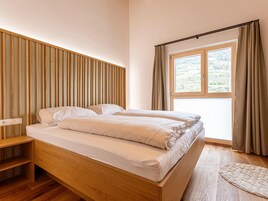 Un dormitorio con cabecera de madera, cama con ropa de cama blanca, una mesita de noche y una ventana con cortinas.