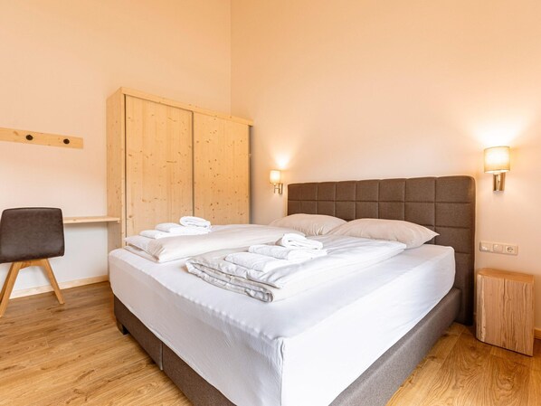 Ein ordentlich bezogenes Bett mit weißen Leinen und Handtüchern, ein Holzschrank, ein kleiner Nachttisch aus Holz und ein Stuhl.
