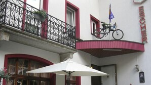 A building with a balcony, a bicycle, and outdoor seating with umbrellas. - Hotel Escher (Leukerbad)