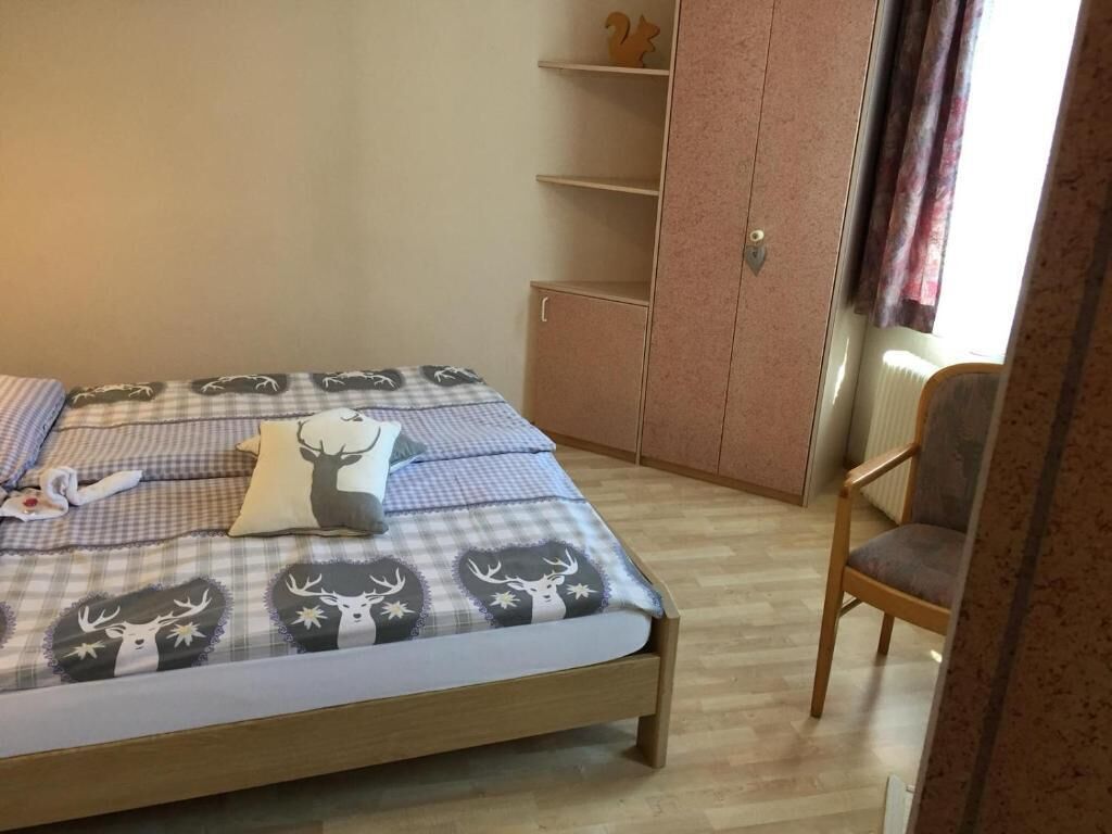 A bedroom with a bed, a chair, a wardrobe, and a window with curtains.