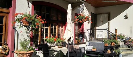 An outdoor seating area with tables and chairs, surrounded by potted plants and flowers.