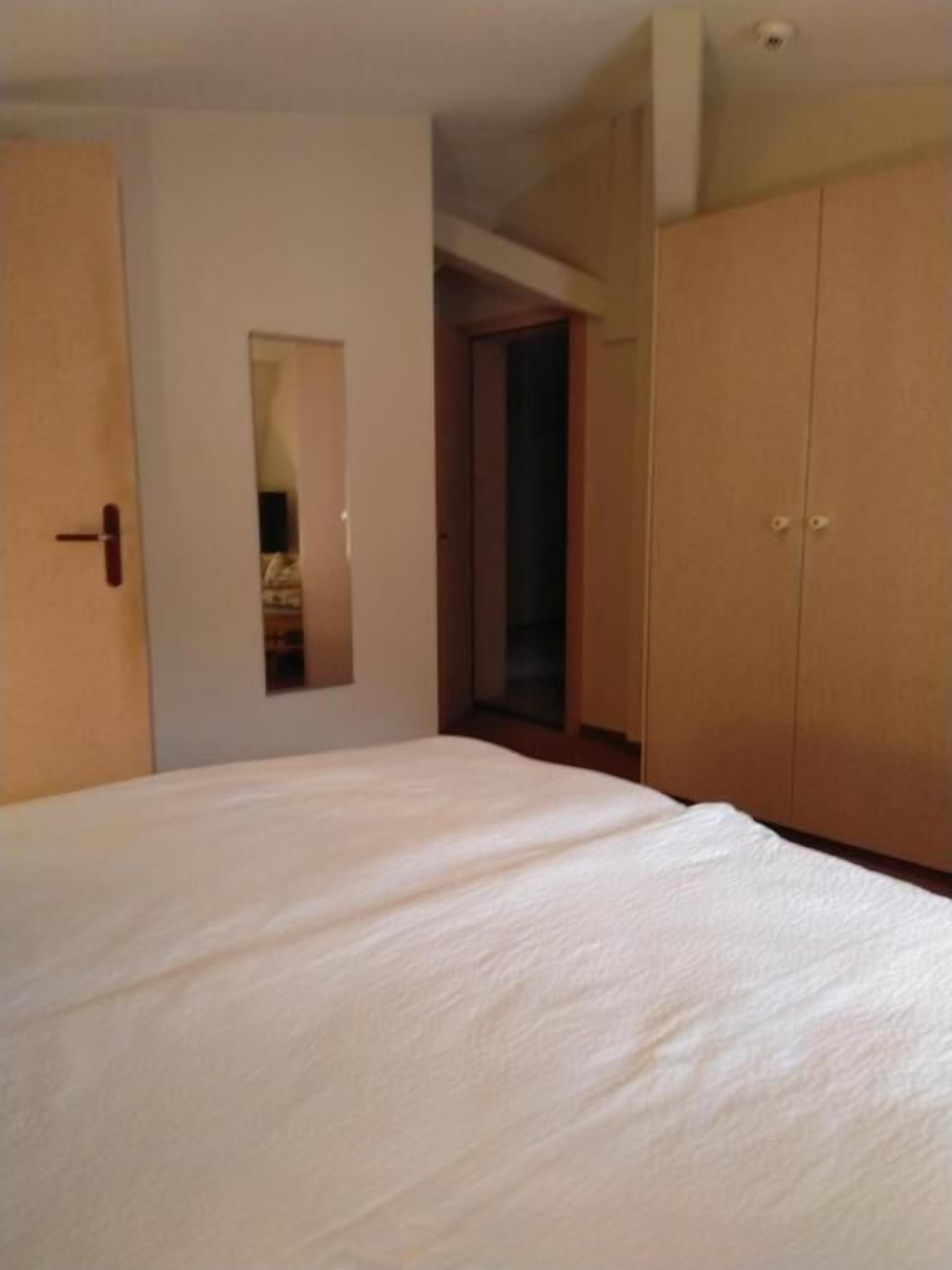 A bedroom with a large bed, a wardrobe, and a door leading to another room.