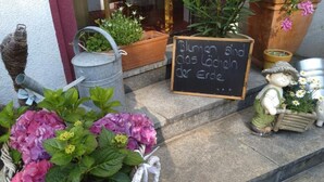 A stone staircase leading to a building entrance, with a metal watering can, a wicker basket with pink flowers, a chalkboard sign, and a garden gnome. - Hotel Escher (Leukerbad)