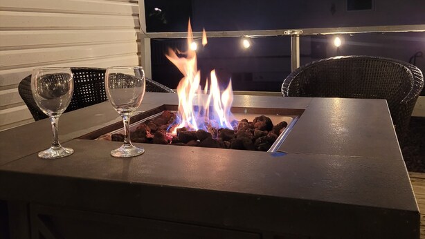 A patio with a fire feature, a glass table, and a wicker chair.