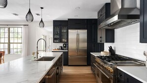 A modern kitchen with a large island, stainless steel appliances, and black cabinetry. - La Mariposa ~ Grand Oasis Big Luxury Home (Sunset Valley Austin)